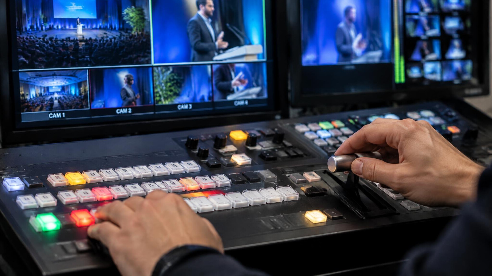 Hands operating a vision mixer switcher panel with multiple preview monitors